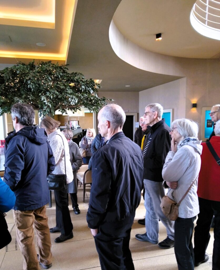 A group of men and ladies listening to the guide in the hotel.