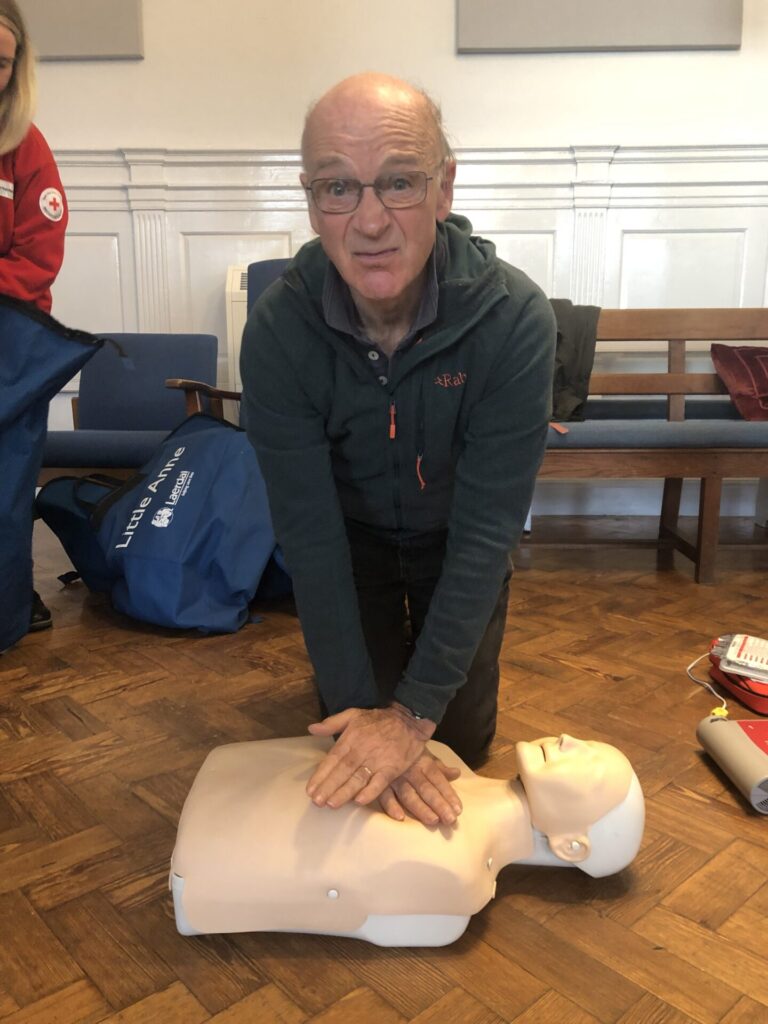 A gentleman on his knees on the floor demonstrating resuscitation on a special dummy.