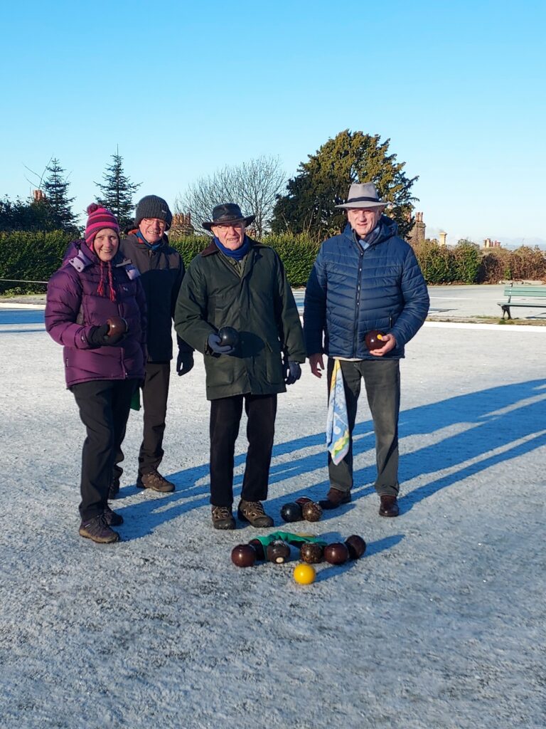 Intrepid bowlers bowling in the frost. A beautiful sunny, though cold day. Their bowls are in the ground in front of them with a yellow jack.