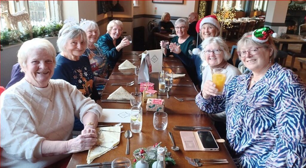 The group at their Christmas lunch, raising a glass. Bright clothes and lots of happy faces.