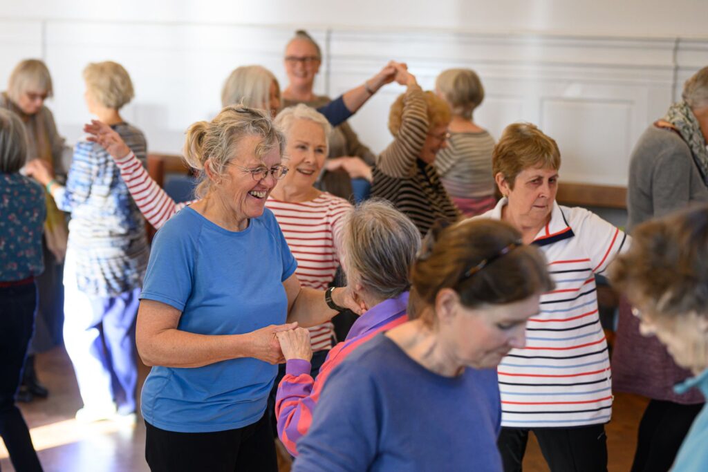 A group of mainly ladies dancing salsa together, happy faces and it's obvious people are really enjoying themselves.