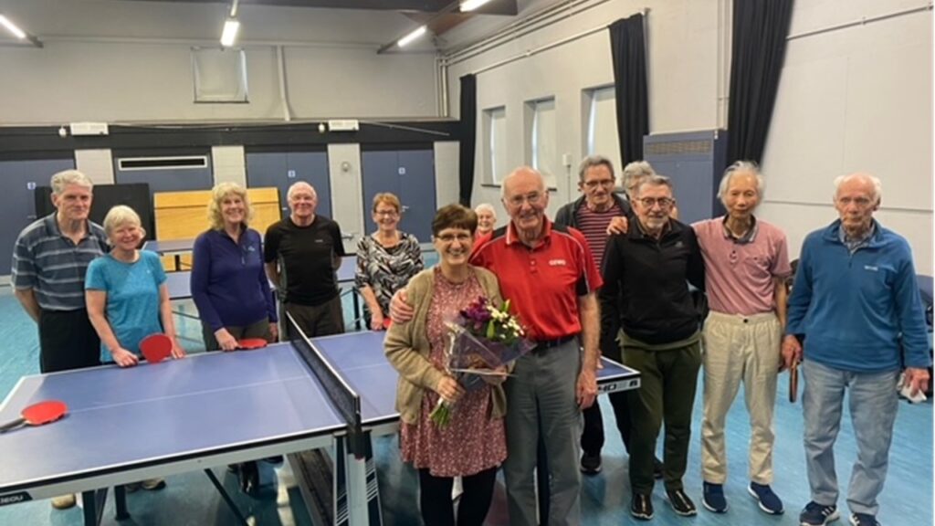 Presentation of a bouquet to the centre's warden. Members of the group standing round the table tennis table with their bats.