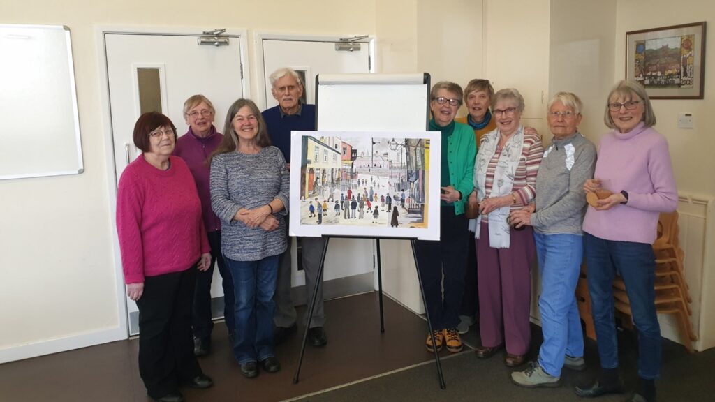 A group of members of the Art Improvers Group with their version of a Lowry painting with 35 people in the foreground.