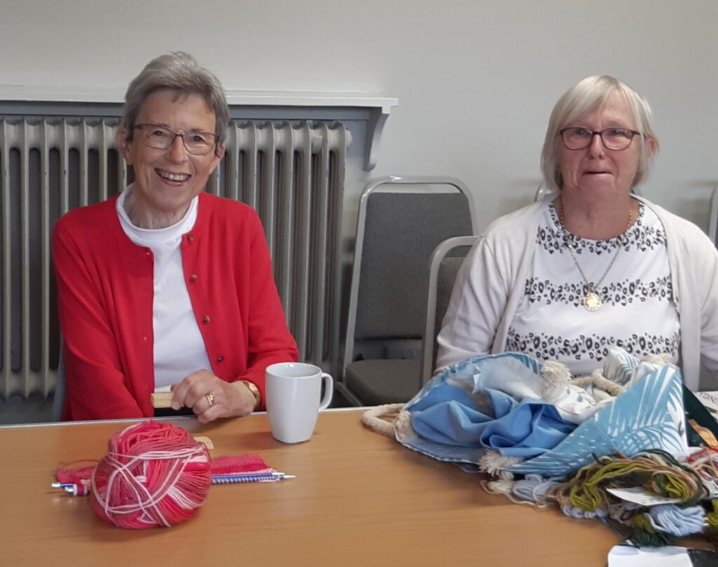 Two ladies enjoying refreshments before carrying on with their knitting and sewing.