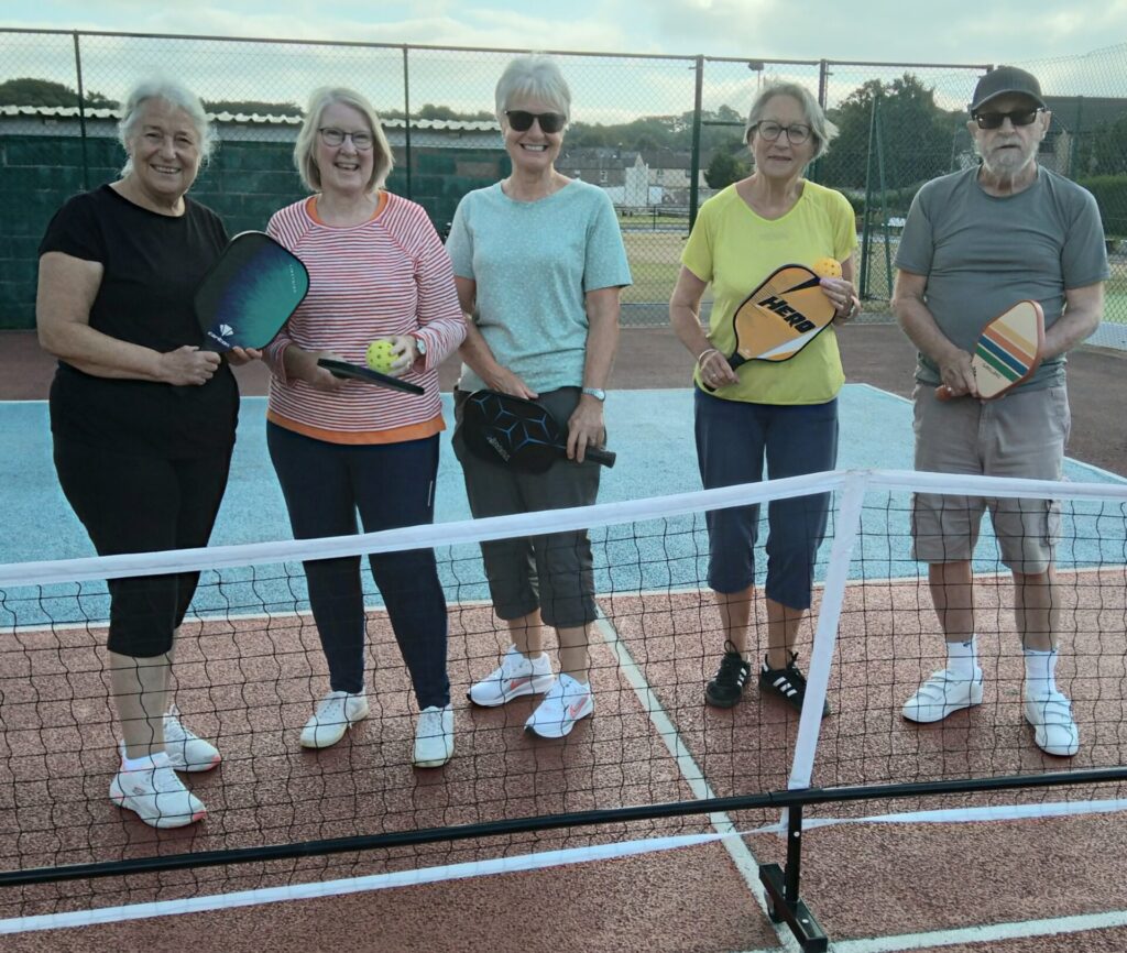 5 members of Pickleball in front of the net.